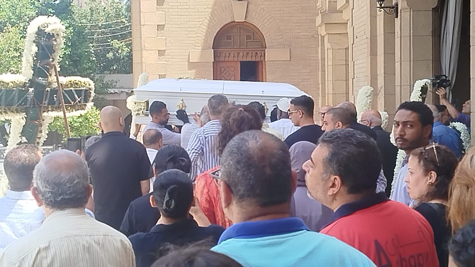 في تابوت أبيض.. نعش الفنان لطفي لبيب محمولا على الأعناق بكنيسة مارمرقس