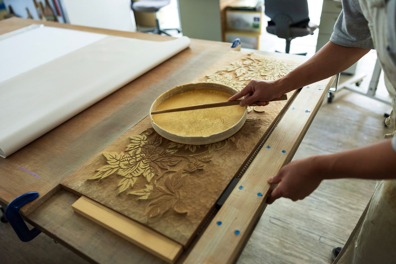 يُوضع الصبغ برفق على السطح البارز للقالب الخشبي باستخدام منخل مغطى بالقماش.(© كاواموتو سايّا)